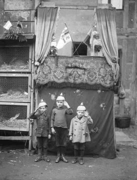 Black and white photo featuring 3 children in front of a puppet show